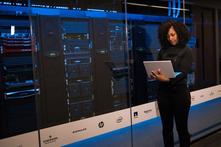 Woman with laptop standing in front of a stack of computer servers.