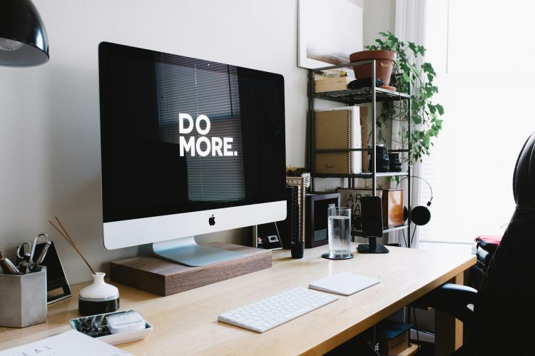 An organized desk with a large iMac that says "Do More" on the screen.