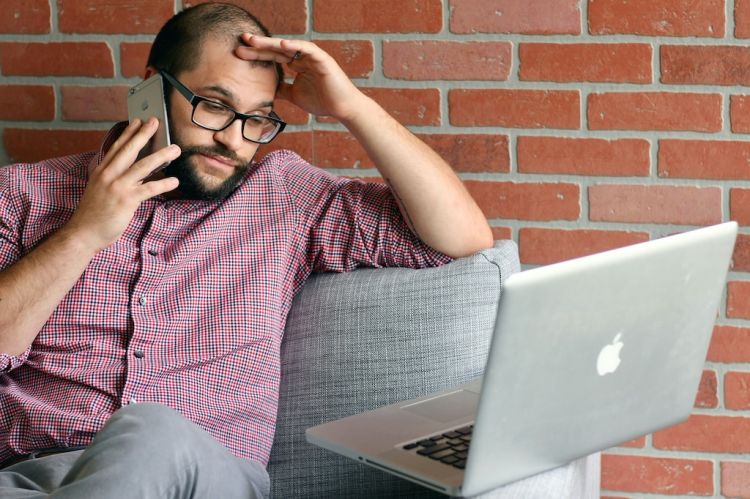 a man looking at a laptop while talking on the phone
