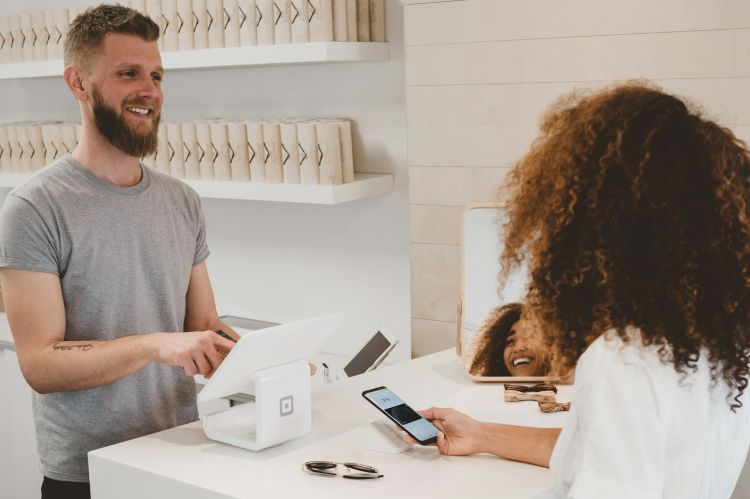 A cashier smiling at a customer who is using her phone to pay at the counter.