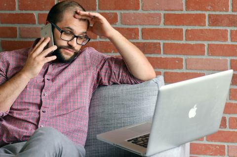 a man looking at a laptop while talking on the phone