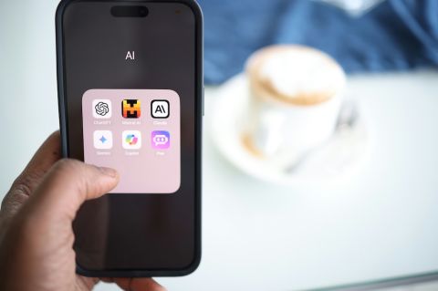 a person holding up a phone. the phone screen displays the icons of several AI apps such as ChatGPT, Gemini and Copilot.