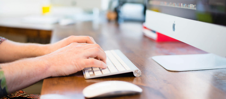 Typing on a keyboard in front of computer screen.